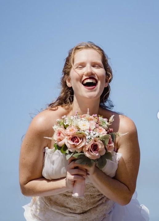Lachende bruid met bloemen tegen een blauwe lucht
